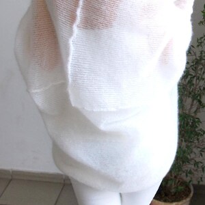 May include: A white, oversized, open-weave sweater. The sweater has a loose, flowing design and is paired with white pants. The image shows the back of the sweater, highlighting its texture and drape. The sweater appears soft and comfortable.