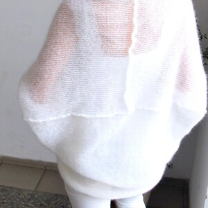 May include: A white, oversized, open-weave knit sweater. The sweater has a wide, flowing design with a layered effect. The model is wearing white pants. The sweater is made of a soft, lightweight material.