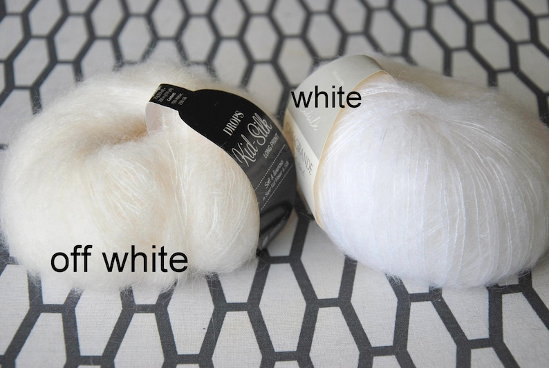 May include: Two skeins of Drops Kid-Silk yarn, one off-white and one white, are displayed against a geometric patterned background. The off-white skein has a black label. The word "white" is written on the white skein.