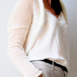 May include: A cream-colored, open-front cardigan with long sleeves. The cardigan is worn over a white top with a lace trim neckline. The person is wearing gray plaid pants with a black belt. The outfit is simple and elegant.