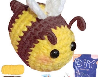 Peut inclure: Un jouet abeille crocheté à rayures jaunes et marron, avec des yeux noirs et des ailes blanches. L'image présente un kit de crochet DIY, comprenant du fil, des aiguilles et un patron. Le kit est pour créer une peluche abeille.