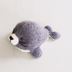 May include: A gray crocheted seal plush toy with white accents around the eyes, nose, and flippers.
