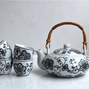 Può includere: Una teiera bianca con un motivo floreale nero e un manico in bambù marrone, insieme a quattro tazze da tè abbinate.