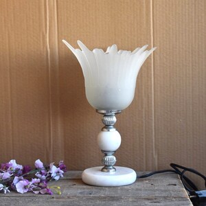 May include: White frosted glass table lamp with a flower-shaped shade and a white marble base. The lamp has a silver metal stem and a silver metal base.