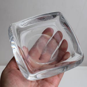 Puede incluir: Un plato cuadrado de vidrio transparente con bordes redondeados. El plato está vacío y parece estar hecho de vidrio grueso.