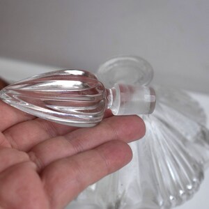 May include: A clear glass bottle with a decorative, fluted stopper. The bottle has a scalloped design and is perfect for holding perfume or essential oils.