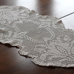 May include: A delicate, off-white crocheted table runner with a scalloped edge and intricate floral pattern.