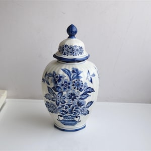 Pode incluir: Um pote de gengibre de cerâmica branca com tampa removível, apresentando um padrão floral azul e ilustrações de pequenos pássaros. O pote tem uma textura vertical canelada e um formato arredondado, com um design floral azul e branco na tampa.