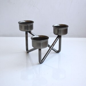 May include: A silver metal candle holder with three candle cups. The holder has a geometric design and is made of sturdy metal.