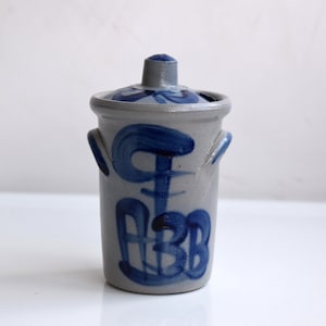 Könnte beinhalten: Eine graue Keramikdose mit Deckel, verziert mit blauen, gemalten Wirbeln und den Buchstaben "ABB".