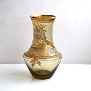 May include: A brown glass vase with a gold rim and floral design. The vase has a wide base and a narrow neck.