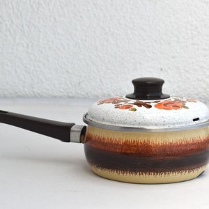 Könnte beinhalten: Ein vintage brauner und weißer Emaille-Topf mit einem Blumendesign auf dem Deckel. Der Topf hat einen braunen Griff und einen silbernen Rand.