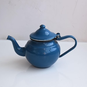 Puede incluir: Una tetera de esmalte azul con cuerpo redondeado, boquilla curva y tapa a juego. El asa tiene un diseño simple y curvo. La tetera es de color azul liso y brillante, con un borde blanco alrededor de la tapa.