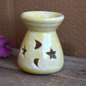 Puede incluir: Un quemador de aceite de cerámica amarillo con un esmalte craquelado blanco y diseños recortados de estrellas y medias lunas.