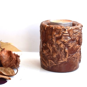 May include: A brown candle holder with a textured surface and a small white candle inside.