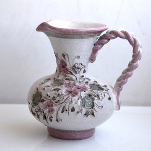 Könnte beinhalten: Eine weiße Keramikkanne mit einem rosafarbenen Blumendesign und einem gedrehten rosafarbenen Henkel.
