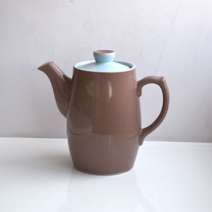 以下が含まれることがあります： 薄い青色の蓋が付いた茶色の陶器製のティーポット。ティーポットは丸みを帯びたボディと側面に注ぎ口があります。取っ手は注ぎ口の反対側にあります。
