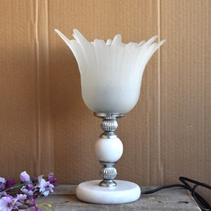 May include: A white table lamp with a frosted glass shade shaped like a flower. The lamp has a silver base with a white marble base.