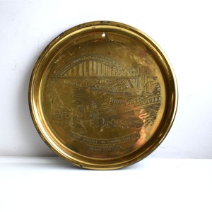 Może przedstawiać: Mosiężna tabliczka ścienna z grawerowanym obrazem mostu Tyne w Newcastle w Anglii. Tabliczka zawiera napis "The Prince of Wales Bridge, Newcastle".