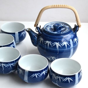 Puede incluir: Un juego de t&eacute; azul y blanco con una tetera y cinco tazas. La tetera tiene un dise&ntilde;o de bamb&uacute; y un asa de madera. Las tazas tambi&eacute;n est&aacute;n decoradas con un dise&ntilde;o de bamb&uacute;.