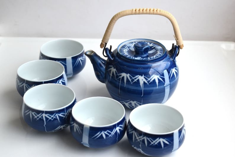 Puede incluir: Un juego de t&eacute; azul y blanco con una tetera y cinco tazas. La tetera tiene un dise&ntilde;o de bamb&uacute; y un asa de madera. Las tazas tambi&eacute;n est&aacute;n decoradas con un dise&ntilde;o de bamb&uacute;.