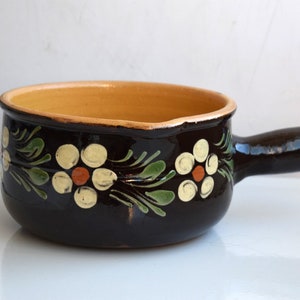 Peut inclure: Un pot en céramique brun avec une poignée, décoré de fleurs blanches et de feuilles vertes. Le pot a un glaçage jaune à l'intérieur.