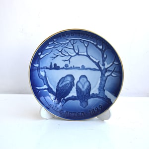 May include: Blue and white porcelain plate with a gold rim. The plate features a winter scene with two birds and the text "1895-1995  Mælstrøm  1895".