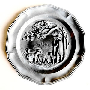 Puede incluir: Un plato de peltre plateado con un diseño en relieve de un pastor con un perro y ovejas bajo un árbol.