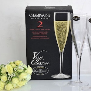May include: A set of two clear champagne flutes with a box of champagne glasses and a bouquet of yellow roses. The box is black with the words "CHAMPAGNE" and "18.5 cl - 6 1/2 oz" printed on it.