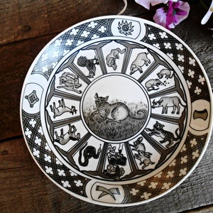 Può includere: Un piatto in ceramica bianca con un design in bianco e nero degli animali dello zodiaco cinese. Il piatto ha un motivo geometrico in bianco e nero attorno al bordo.