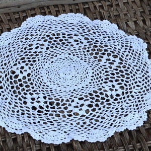 May include: White crocheted doily with a circular design. The doily has a delicate, intricate pattern and is made of fine thread.