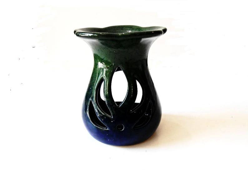 May include: A blue and green ceramic oil burner with a decorative cutout design. The burner has a wide, flat top and a rounded base.