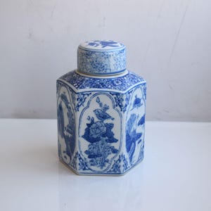 May include: A blue and white porcelain tea caddy with a hexagonal shape and a matching lid. The caddy features detailed illustrations of birds and flowers. The design is a classic example of Asian-inspired ceramics.