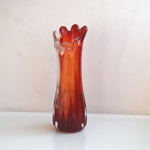 May include: A red and orange glass vase with a ruffled top and a textured surface.