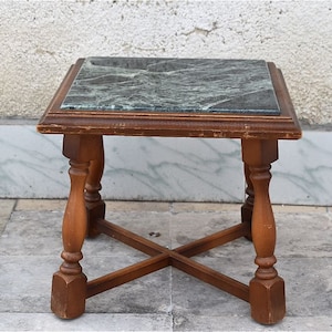 May include: A small, square, wooden end table with a green marble top. The table has four turned legs and a cross-shaped base.