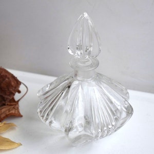 May include: A clear glass bottle with a decorative, fluted design and a pointed stopper. The bottle is empty and has a vintage look.