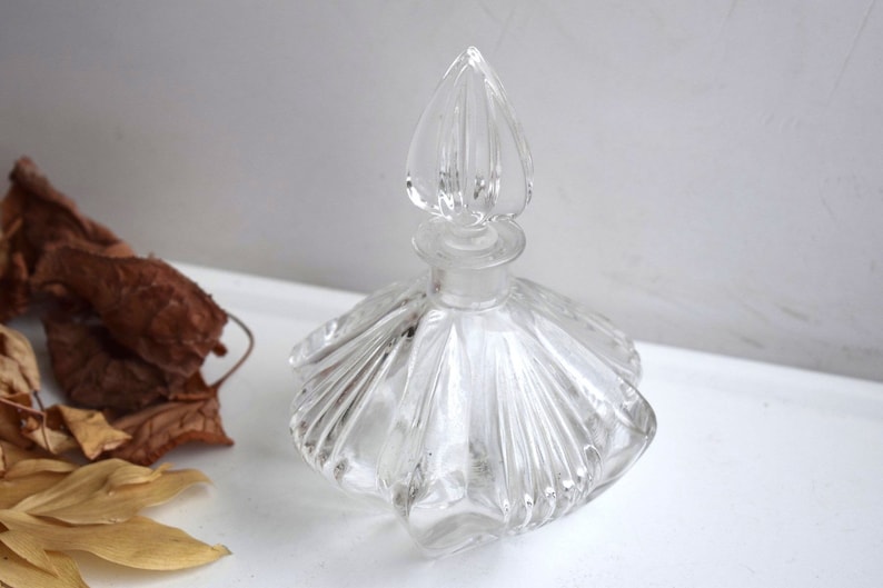May include: A clear glass bottle with a decorative, fluted design and a pointed stopper. The bottle is empty and has a vintage look.