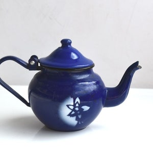 Puede incluir: Una tetera de esmalte azul con un diseño floral blanco. La tetera tiene una tapa y un pico.