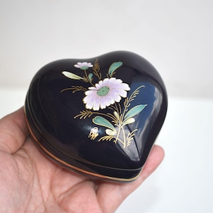 Può includere: Una scatola per gioielli a forma di cuore con sfondo blu scuro e un motivo floreale in oro, verde e viola.
