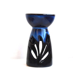 Könnte beinhalten: Ein blauer und schwarzer Keramik-Ölbrenner mit floralem Design. Der Brenner hat oben eine breite, flache Schale und einen Sockel mit ausgeschnittenen Designs.