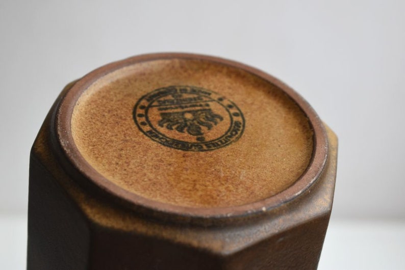 Może przedstawiać: Brązowy, ośmiokątny wazon ceramiczny z czarną pieczątką na spodzie, na kt&oacute;rej widnieje napis "Made in England, Denby Pottery, Made in England".