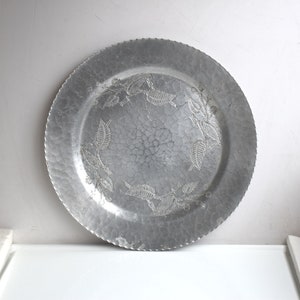 Könnte beinhalten: Ein silbernes Aluminium-Serviertablett mit gehämmerter Oberfläche und einem dekorativen, geprägten Blattdesign am Rand.