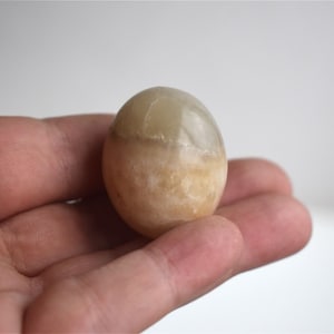 May include: A smooth, round, light brown and white agate sphere. The sphere is about the size of a golf ball.