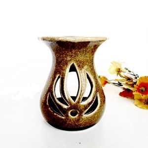 May include: A brown ceramic oil burner with a decorative cutout design. The burner has a wide base and a narrow opening at the top.