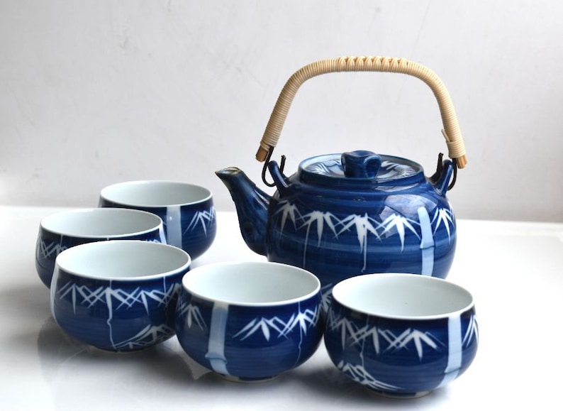 Puede incluir: Un juego de t&eacute; azul y blanco con una tetera y cinco tazas. La tetera tiene un dise&ntilde;o de bamb&uacute; y un asa tejida. Las tazas tambi&eacute;n est&aacute;n decoradas con un dise&ntilde;o de bamb&uacute;.