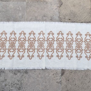 May include: A white rectangular rug with a brown, intricate, repeating pattern. The rug has a fringed edge.