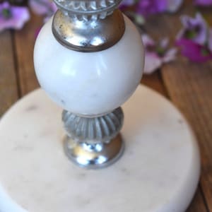 May include: White marble candle holder with a silver base and a decorative top.