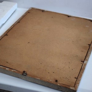 May include: A plain, brown picture frame with a white painted wooden frame. The frame is slightly distressed and has a few small nail holes.