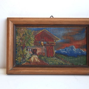 K&ouml;nnte beinhalten: Ein gerahmtes Gem&auml;lde, das ein rotes Haus mit blauem Dach und wei&szlig;en Verzierungen zeigt. Das Haus steht vor dem Hintergrund gr&uuml;ner H&uuml;gel und blauer Berge. Das Gem&auml;lde ist signiert mit "E.W.T. Melzer".