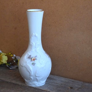 May include: White porcelain vase with a gold rim and floral design. The vase has a bulbous base and a narrow neck.